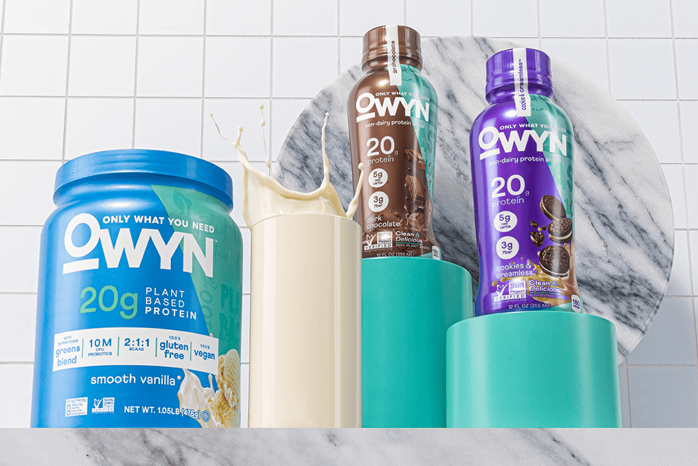 various OWYN products with a glass of milk in marble table and tiles and marble background.
